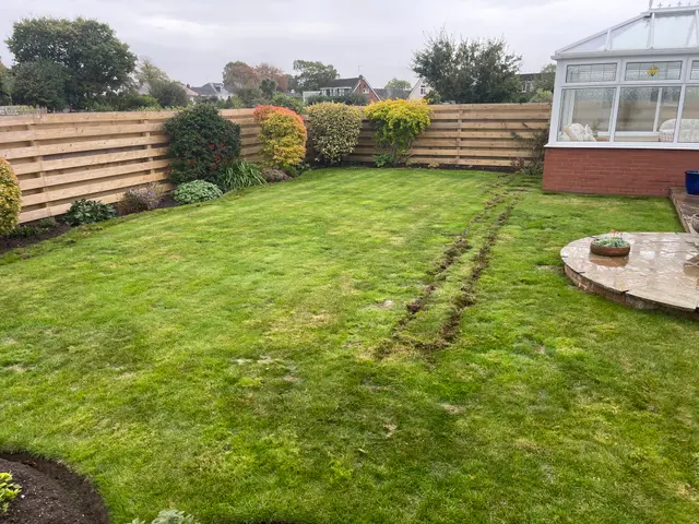 Existing lawn beside planted borders and a conservatory, with initial turf cuts visible