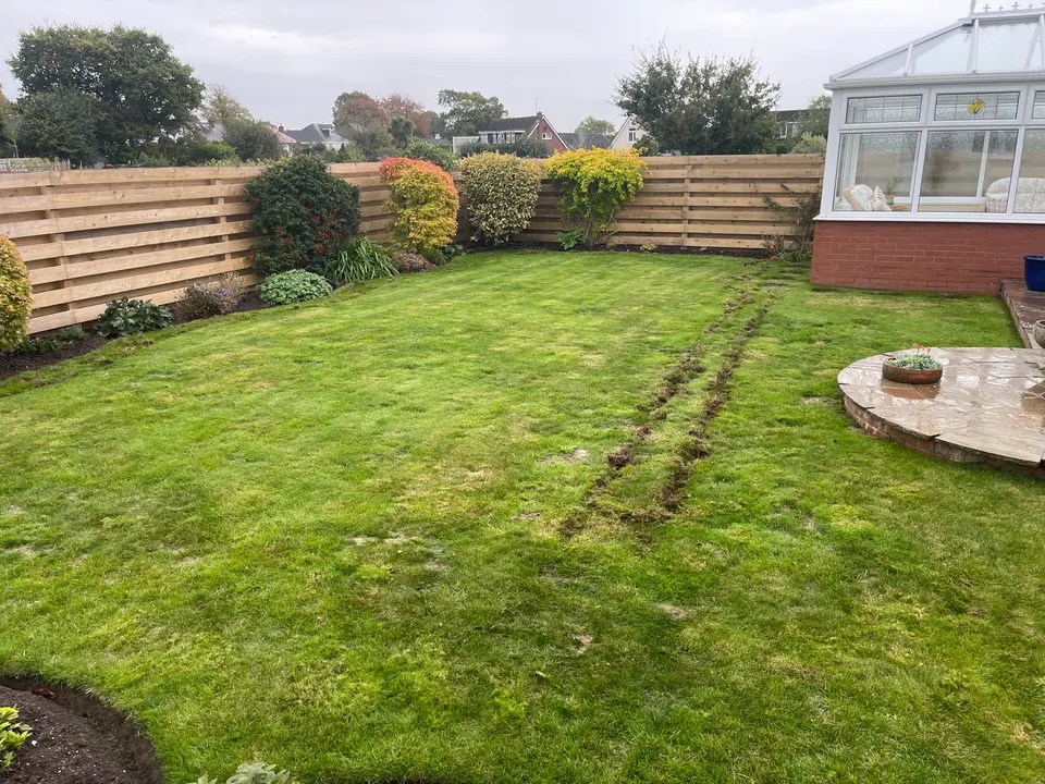 Existing lawn beside planted borders and a conservatory, with initial turf cuts visible